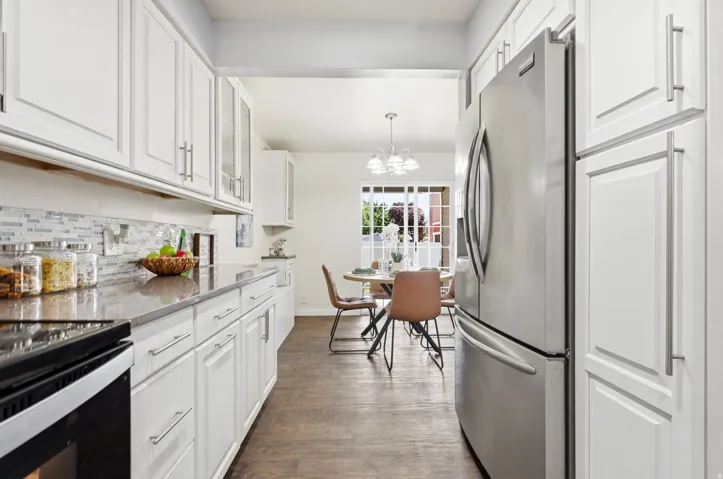 White cabinetry with brushed nickel hardware, stainless steel appliances, mosaic tile backsplash, solid surface countertops, and wood-finish flooring