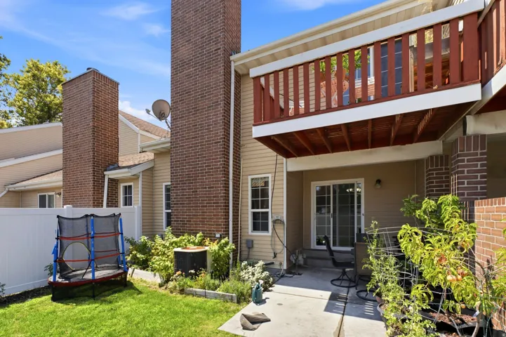 Private outdoor patio with a sliding glass door, a brick column, and an upper-level balcony with a wooden railing