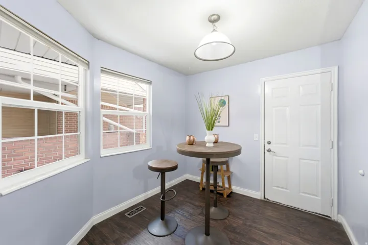 Interior space featuring dark wood-finish flooring, two windows with white blinds, a white paneled door, and a ceiling-mounted pendant light fixture