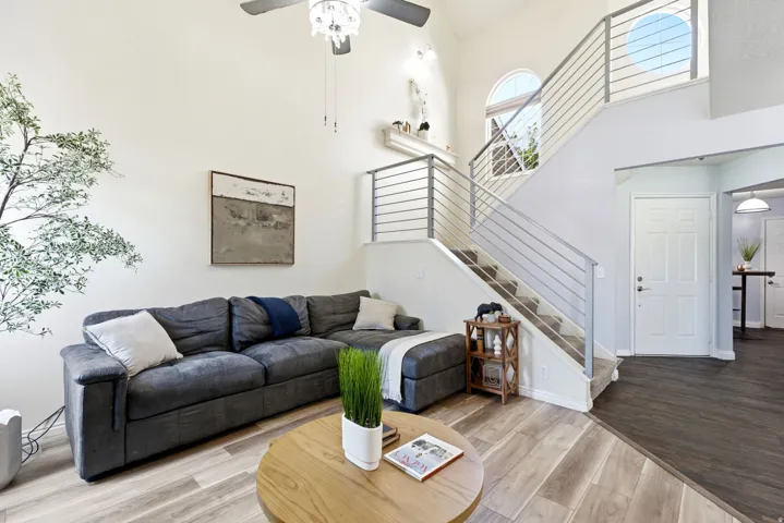 Vaulted ceiling with a ceiling fan, light wood-finish flooring, staircase with metal railings, arched window, and a paneled entry door