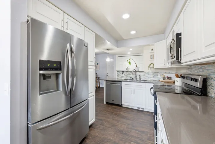 White cabinetry, wood-finish flooring, stainless steel appliances, recessed lighting, and a mosaic tile backsplash