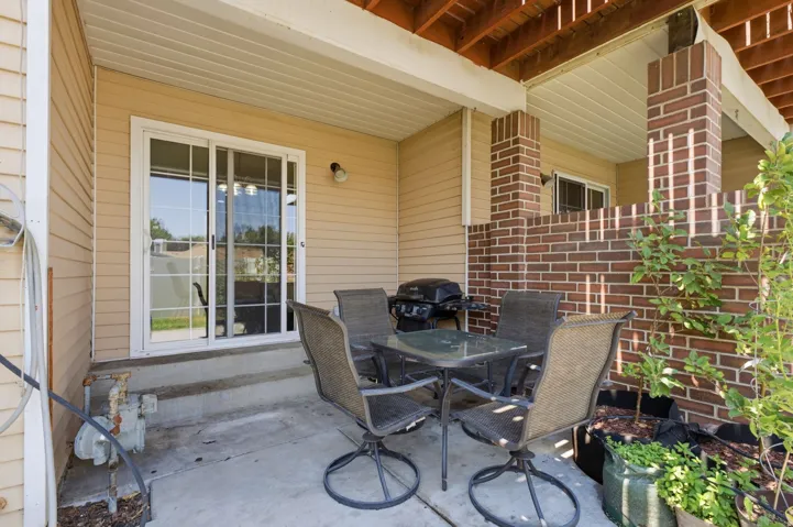 Covered concrete patio with siding exterior, brick columns, and a sliding glass door