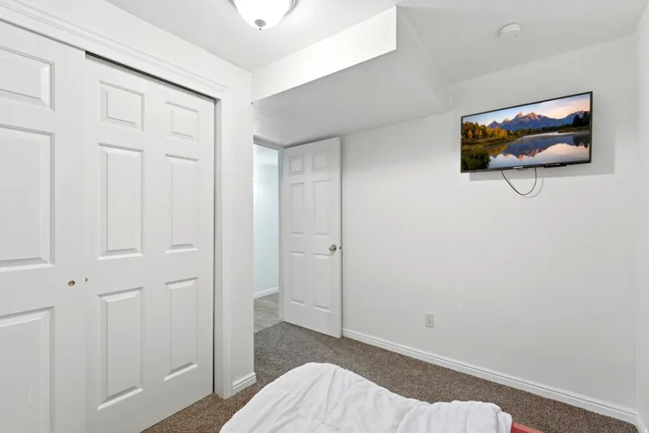 Carpeted flooring, white six-panel bi-fold closet doors, white six-panel interior door, and a flush mount ceiling light fixture