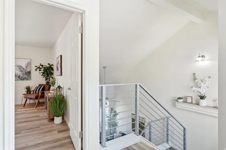 Vaulted ceiling featuring a contemporary wall sconce, wood-finish flooring, and a modern metal railing system