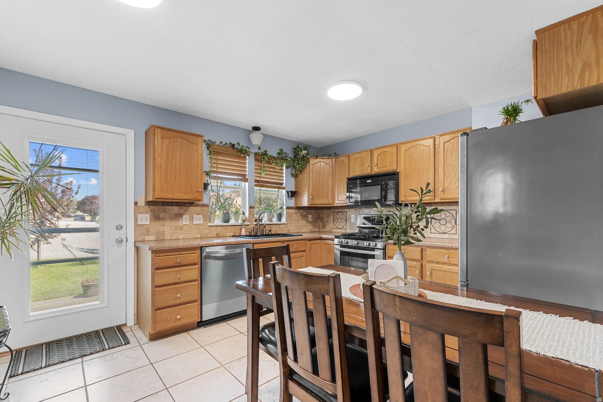 Kitchen featuring wood cabinetry, stainless steel dishwasher, tile backsplash, and tile flooring