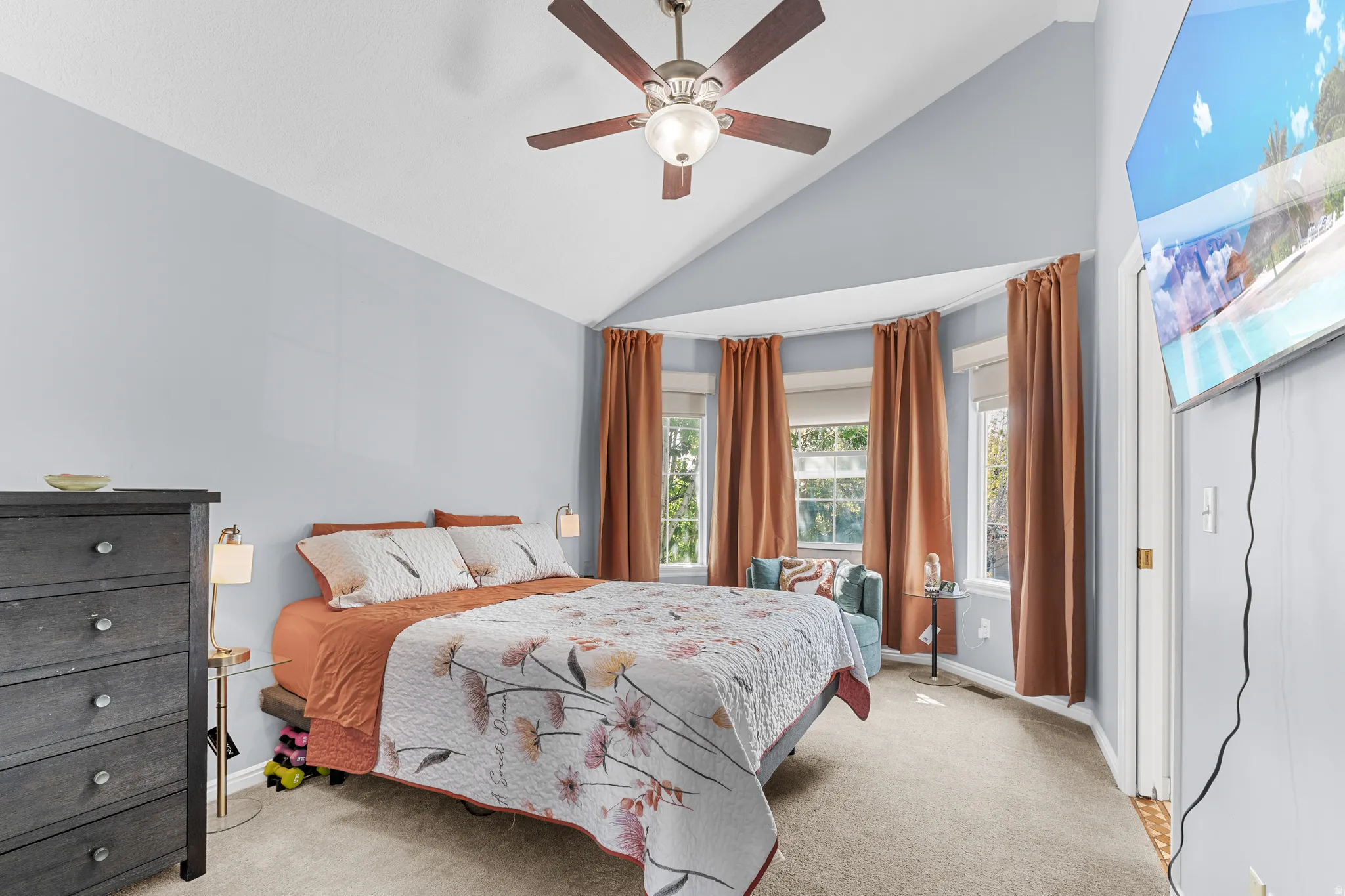 Master Bedroom. Vaulted ceiling with a ceiling fan, bay window with three large windows, carpet flooring, and light blue wall finish