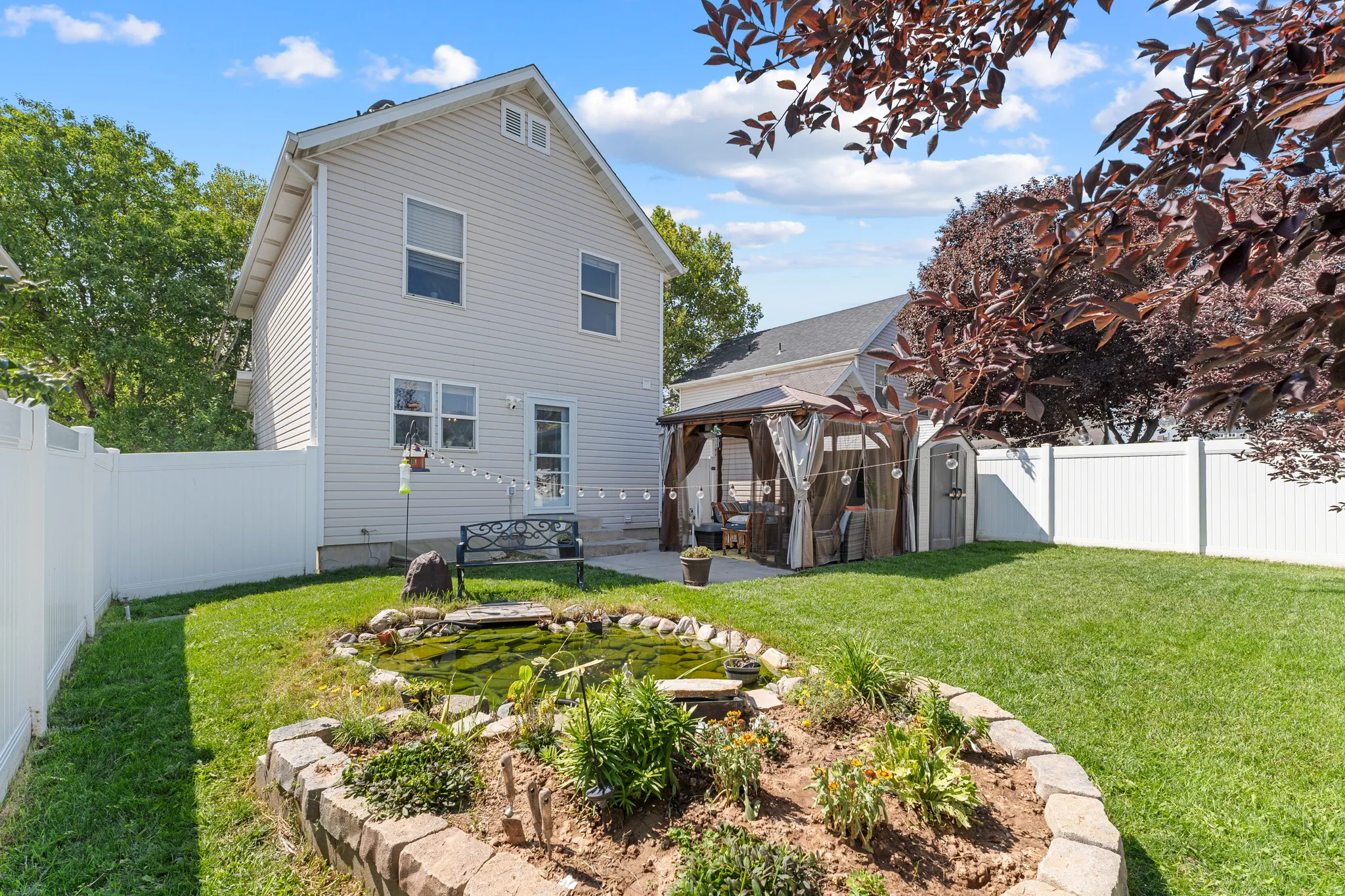 Expansive backyard featuring a manicured lawn, established garden bed with stone edging, and a built-in pond