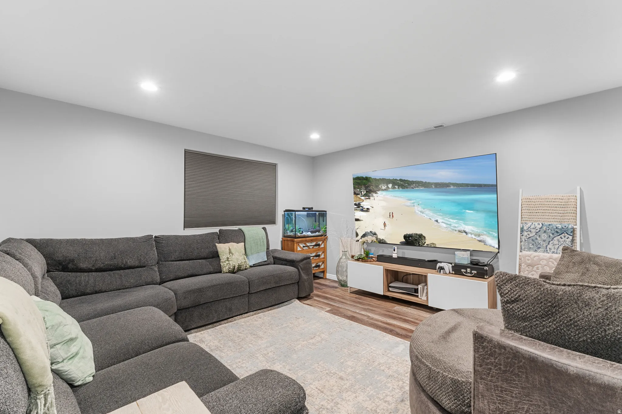Recessed lighting, light gray walls, wood-finish flooring, and a window with a roller shade