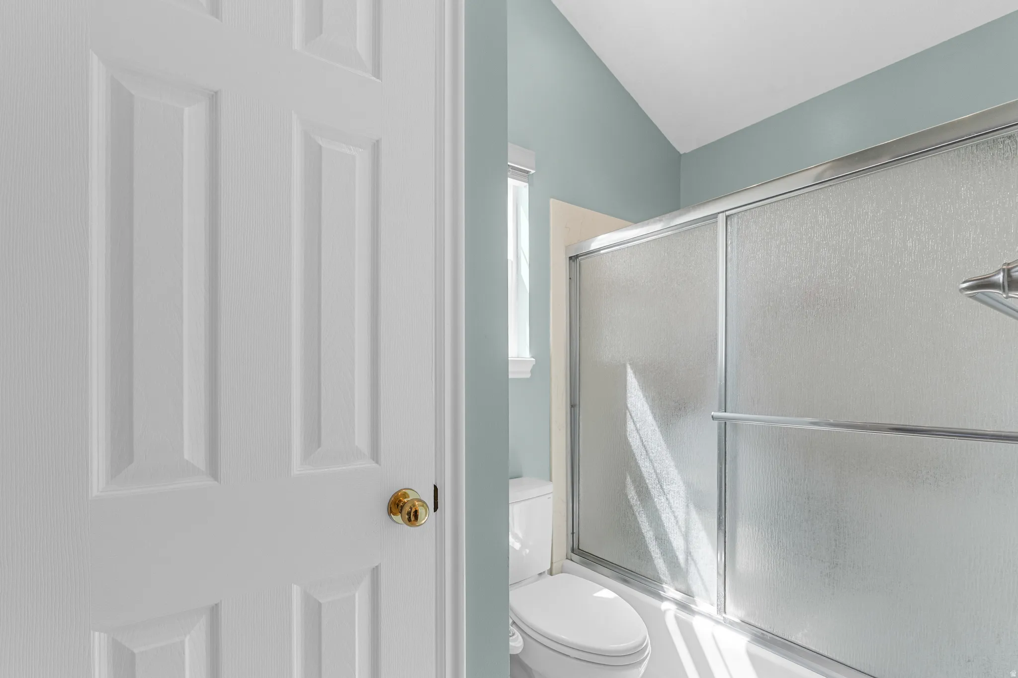 Frosted glass shower enclosure with chrome framing, white toilet, and vaulted ceiling