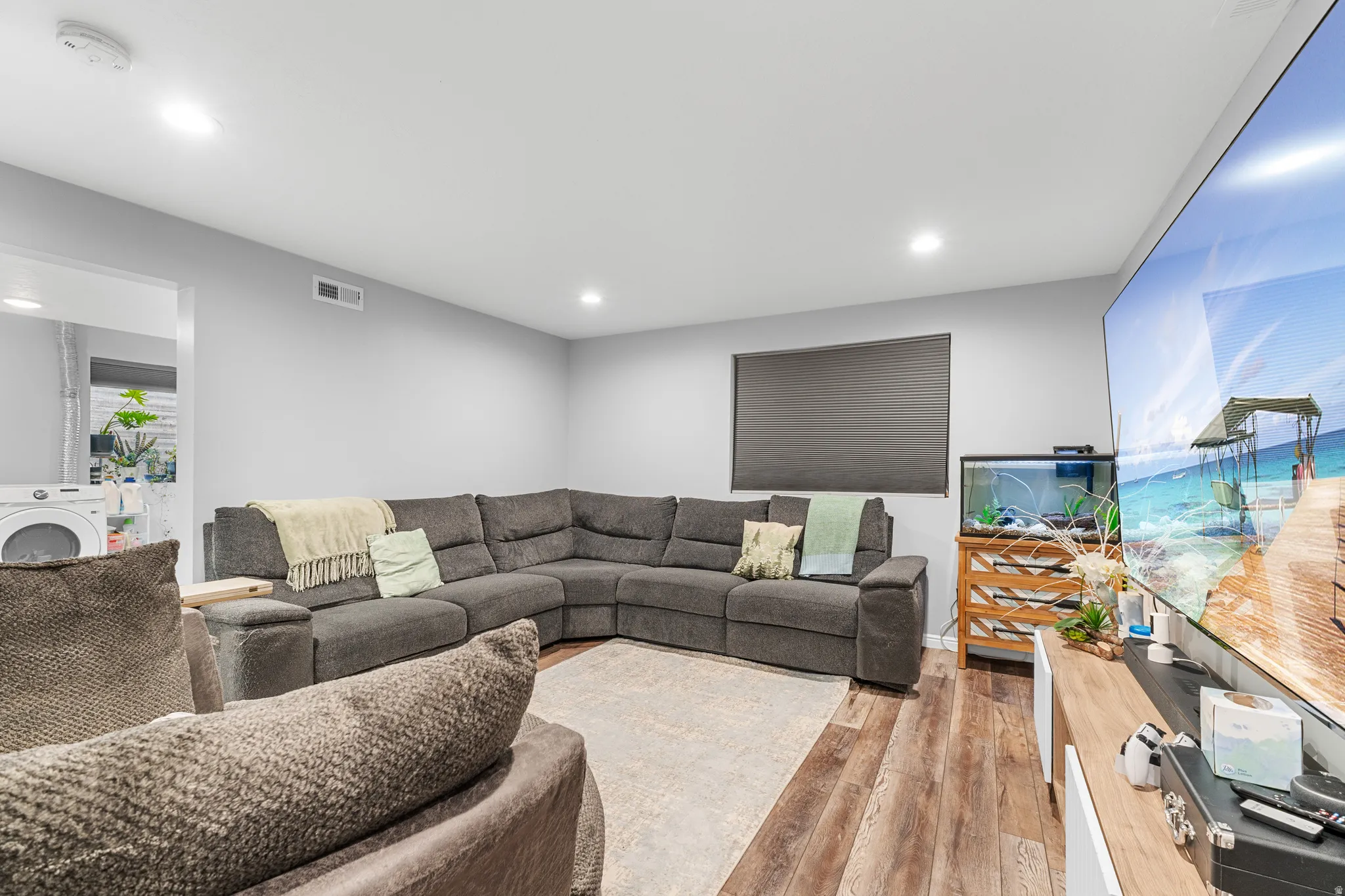 Recessed lighting illuminates the living area featuring wood-finish flooring and light gray painted walls