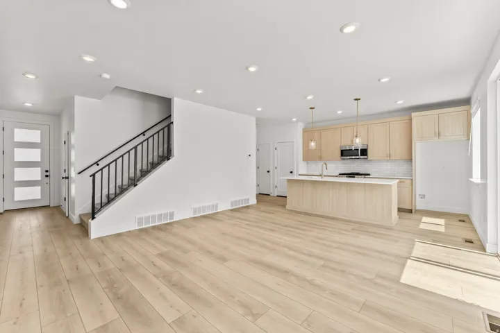 Wood-finish flooring throughout, recessed lighting, modern kitchen cabinetry, integrated kitchen island with sink, and a contemporary staircase with metal balusters