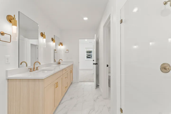 Dual vanity with light wood-finish cabinetry, white countertops, and gold-toned fixtures