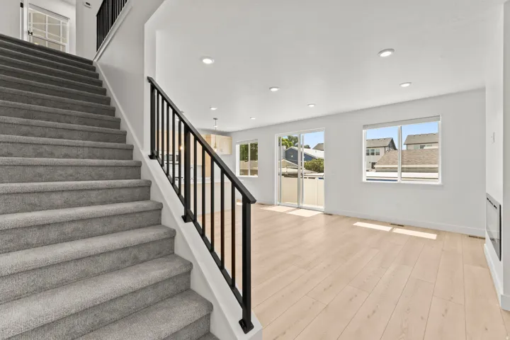 Carpeted staircase with black metal railings, wood-finish flooring, recessed lighting, and a sliding glass door