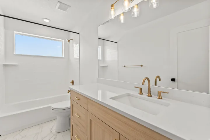 Wood-finish vanity with gold-tone hardware, rectangular undermount sink, and white countertop