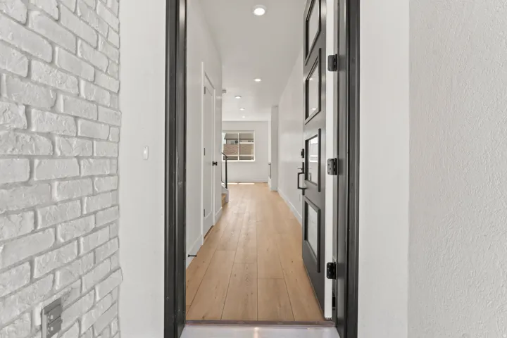 Painted brick wall, dark frame door with multiple glass inserts, wood-finish flooring, recessed lighting, and white walls