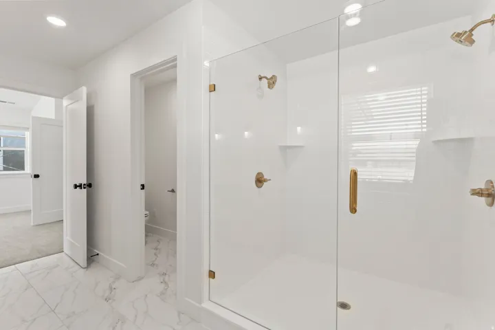 Glass-enclosed shower with brass fixtures, white subway tile, and two built-in shelves