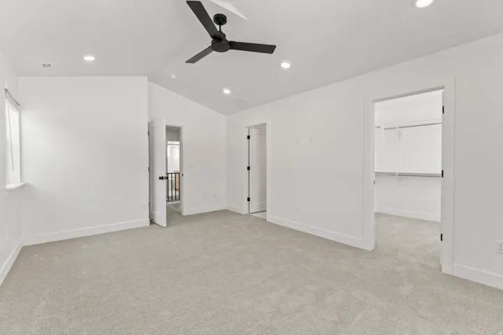 Spacious primary bedroom featuring recessed ceiling lighting, a ceiling fan, neutral carpeting, and multiple closet spaces with white-painted doors and hardware