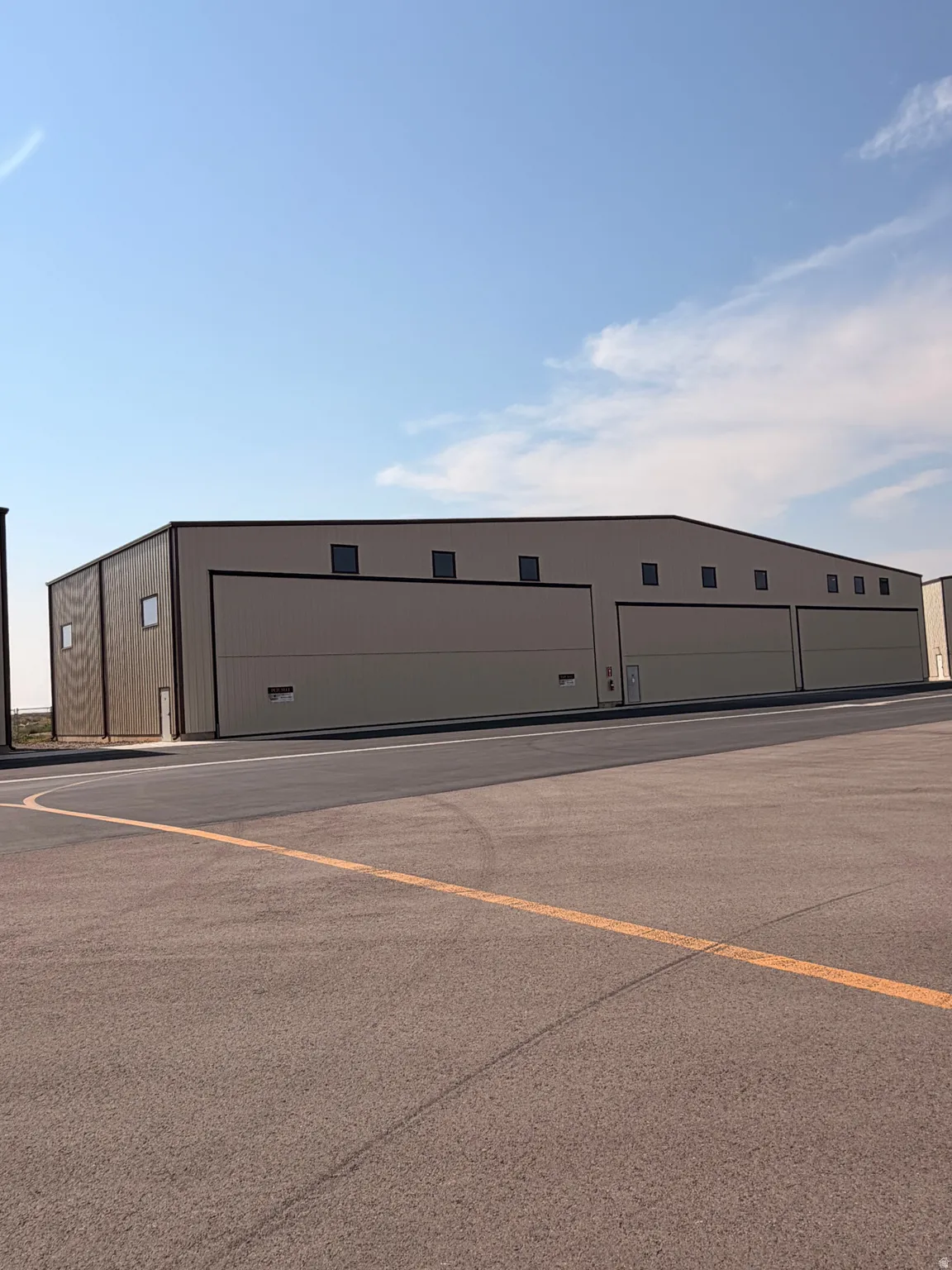 Expansive metal structure featuring multiple large bay doors, upper-level windows, and a surrounding paved surface