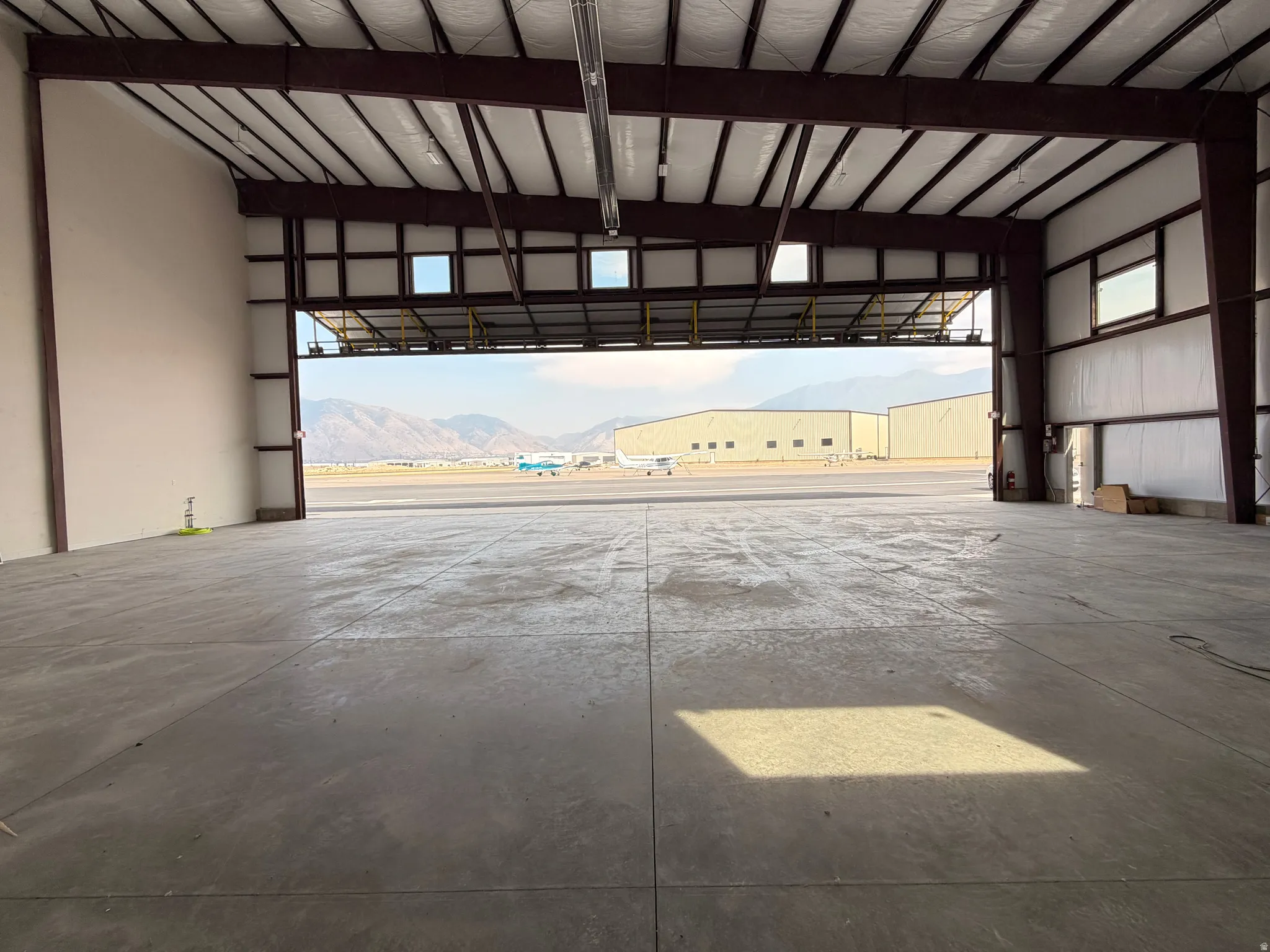 Expansive industrial warehouse featuring a wide-open concrete floor plan, high vaulted ceiling with exposed steel beam structure, and multiple large overhead garage doors with transom windows