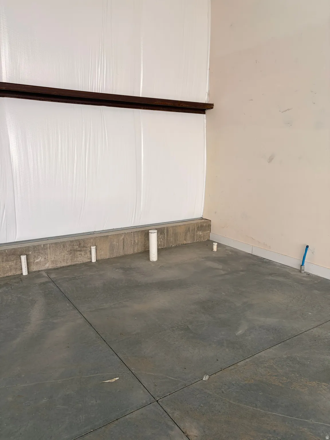 Concrete flooring with visible utility rough-ins, complemented by a partial concrete wall and an upper wooden beam
