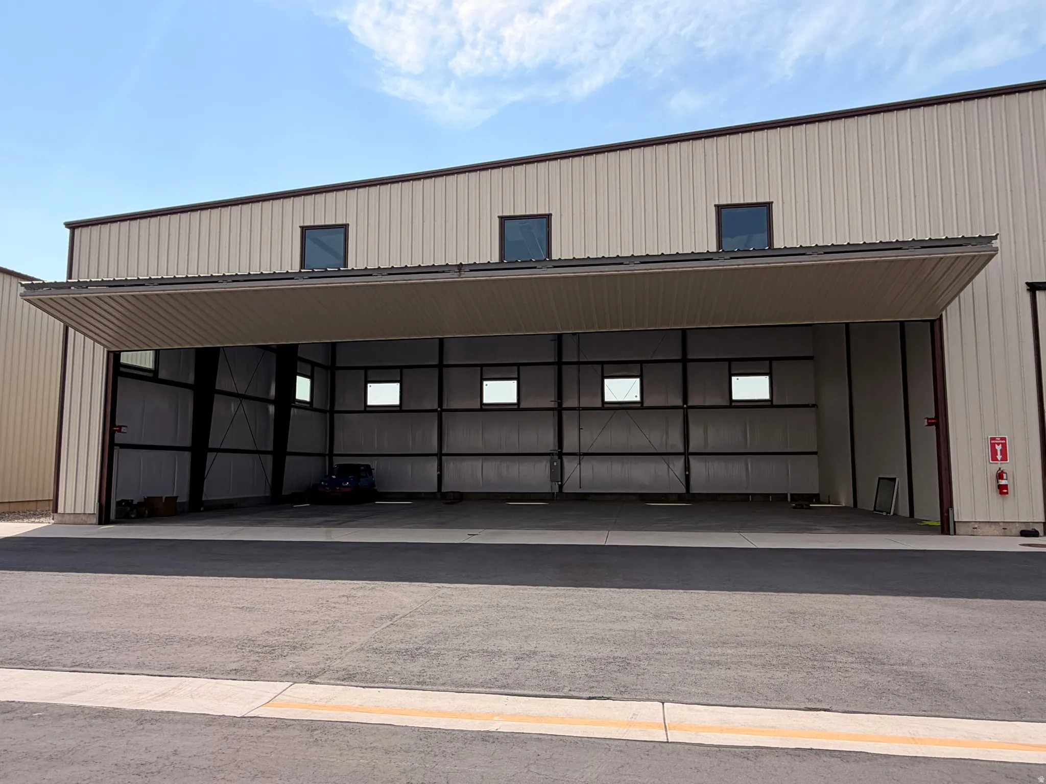 Steel-framed hangar building featuring a bi-fold hangar door, corrugated metal siding, and multiple upper-level windows