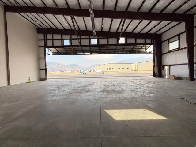 Expansive industrial warehouse featuring a wide-open concrete floor plan, high vaulted ceiling with exposed steel beam structure, and multiple large overhead garage doors with transom windows