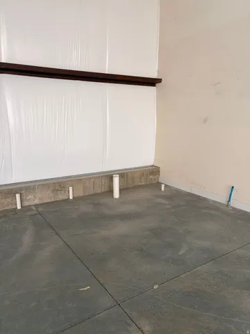 Concrete flooring with visible utility rough-ins, complemented by a partial concrete wall and an upper wooden beam