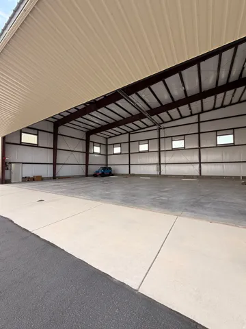 Spacious commercial structure featuring an expansive overhead door, concrete flooring, steel beam construction, insulated walls, and multiple transom windows