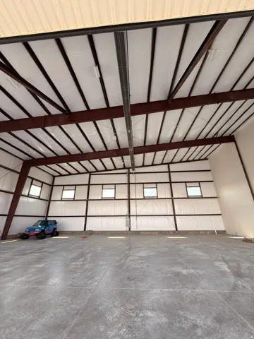 Expansive open-concept interior featuring a high vaulted ceiling with exposed steel beams, insulated walls, concrete flooring, and multiple high windows providing natural light