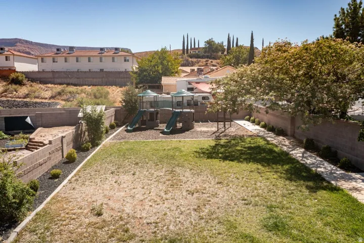 Expansive terraced yard featuring a grass area, concrete block retaining walls, mature trees, and a paved walkway