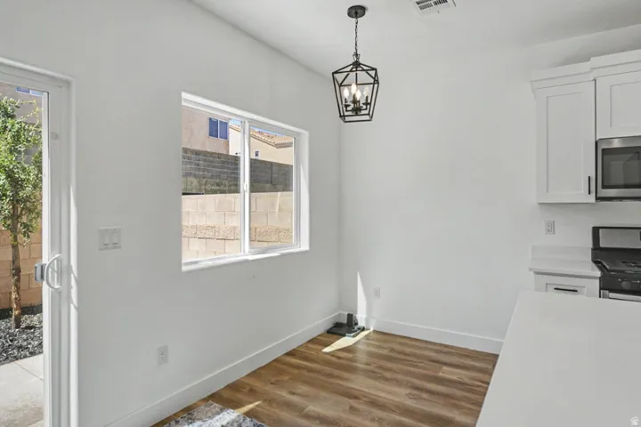 Wood-finish flooring, white cabinetry, stainless steel microwave, stainless steel range, and a pendant light fixture