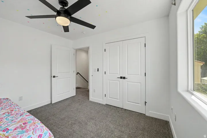 White walls with gray carpeting, featuring a window and a black ceiling fan with integrated lighting