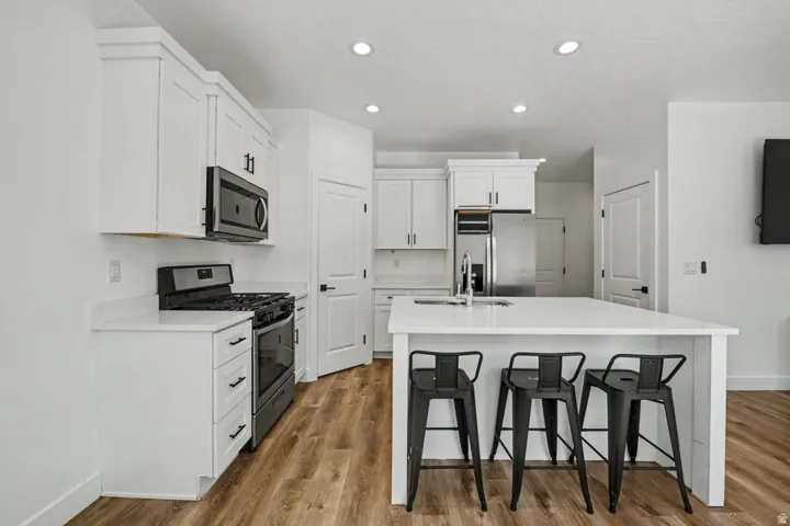 Modern kitchen featuring white cabinetry, stainless steel appliances, a center island with countertop seating, recessed lighting, and wood-finish flooring