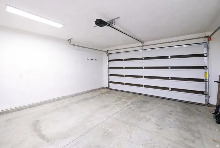 Attached single-bay garage with a concrete floor, white walls, and overhead lighting
