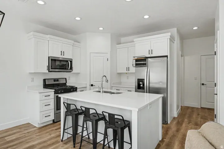White cabinetry, stainless steel appliances, central island with seating, recessed lighting, and wood-finish flooring