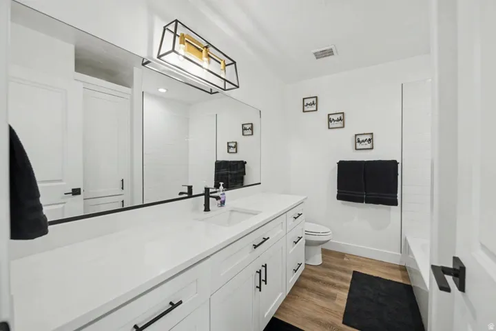 Bathroom featuring an extended vanity with dual sinks, white cabinetry, dark hardware, and wood-finish flooring