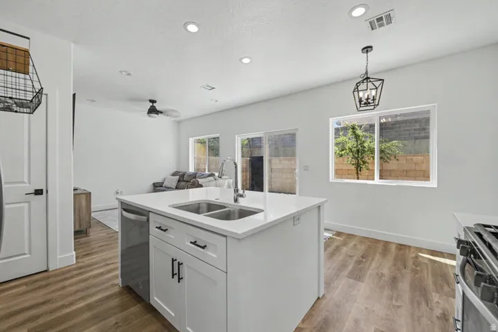Kitchen island with dual sinks, recessed lighting, wood-finish flooring, white cabinetry, and stainless steel appliances