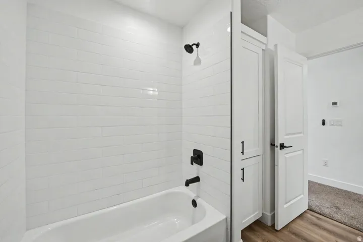 Bathtub with white subway tile surround, matte black shower fixtures, built-in white cabinetry, and a white paneled door