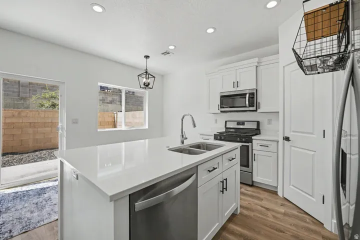 Modern kitchen featuring an expansive island with a stainless steel sink, sleek white cabinetry, stainless steel appliances, and wood-finish flooring