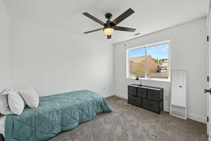 White walls, dark gray carpet, a ceiling fan with light, and a large window