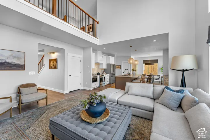 Open-concept living area featuring high ceilings, wood-finish flooring, a kitchen island with pendant lighting, and a second-story overlook with a wood and metal railing