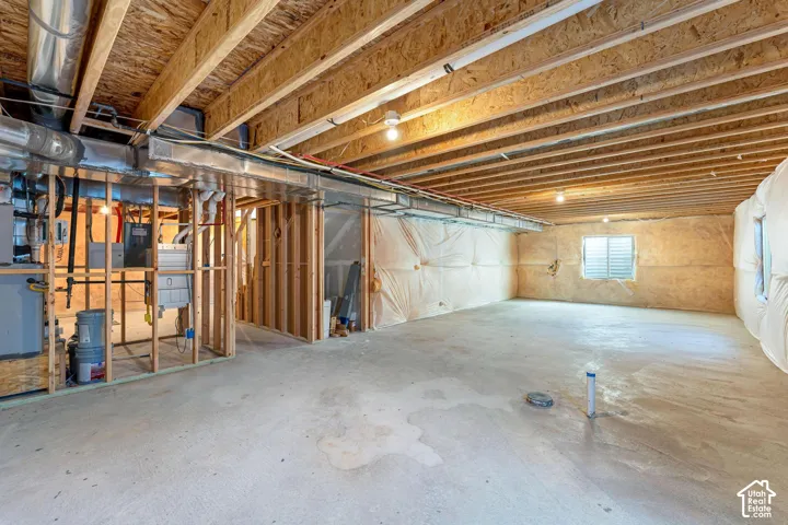 Unfinished basement featuring exposed wood ceiling joists, concrete flooring, and perimeter wall insulation