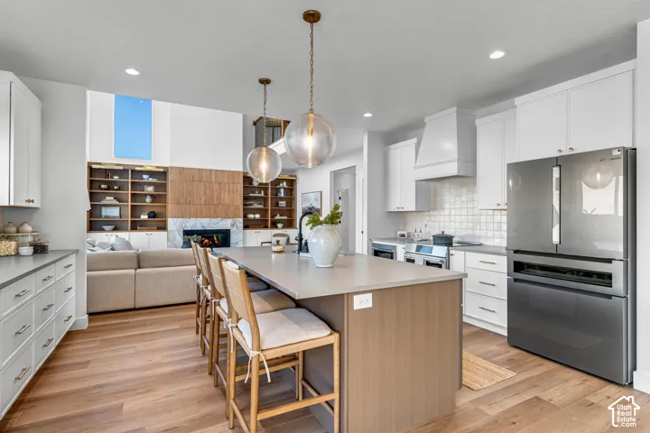 Kitchen island with seating, stainless steel appliances, white cabinetry, wood-finish flooring, and a fireplace with built-in shelving