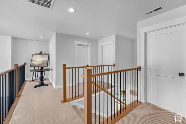 Carpeted hallway featuring a wood-finish and black metal railing, white doors with modern black hardware, and recessed lighting