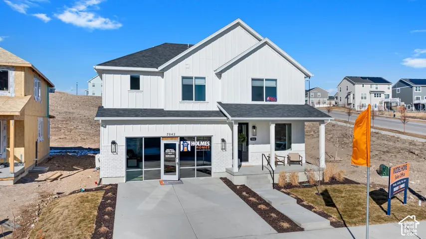 White siding exterior with board and batten accents, black-shingled roof, covered front porch, and a concrete driveway