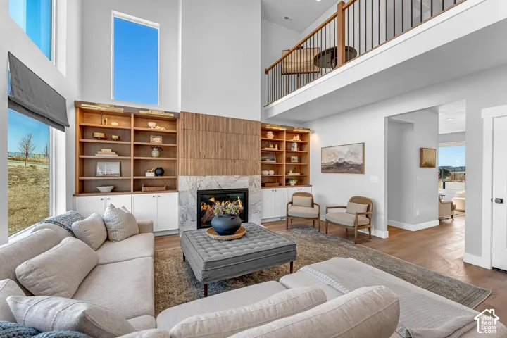 Two-story living area featuring a fireplace with a stone surround, built-in shelving, hardwood flooring, and an upper-level balcony with metal balusters