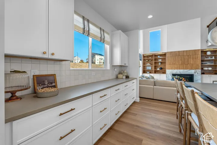 White cabinetry with brass hardware, light wood-finish flooring, a contemporary fireplace with a stone surround, and built-in shelving