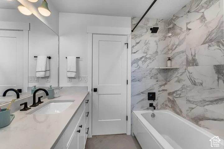 Bathroom featuring a white vanity with an integrated sink, matte black fixtures, a built-in bathtub, and a tiled shower surround with a recessed shelf