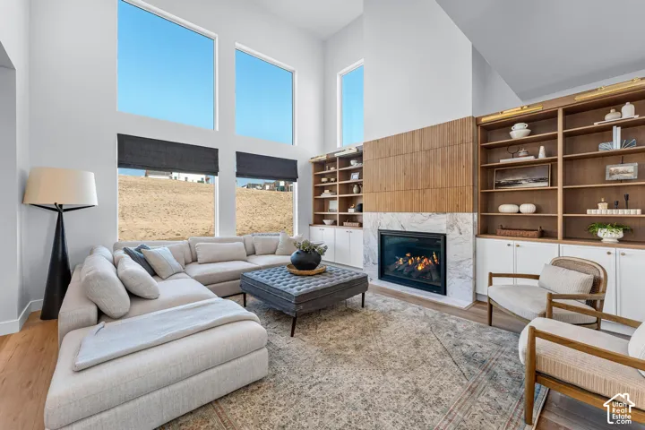 Vaulted ceiling with tall windows, integrated fireplace with marble-style surround, built-in shelving, wood-finish flooring, and recessed lighting