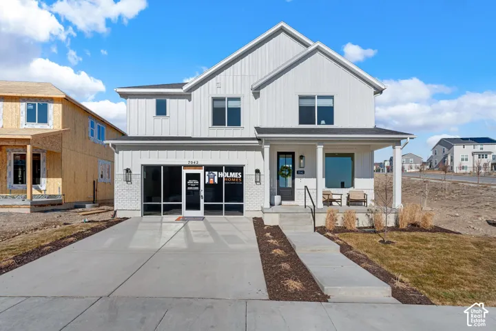 White vertical siding exterior with partial brick facade, covered entry porch, dark-framed windows, and a concrete driveway